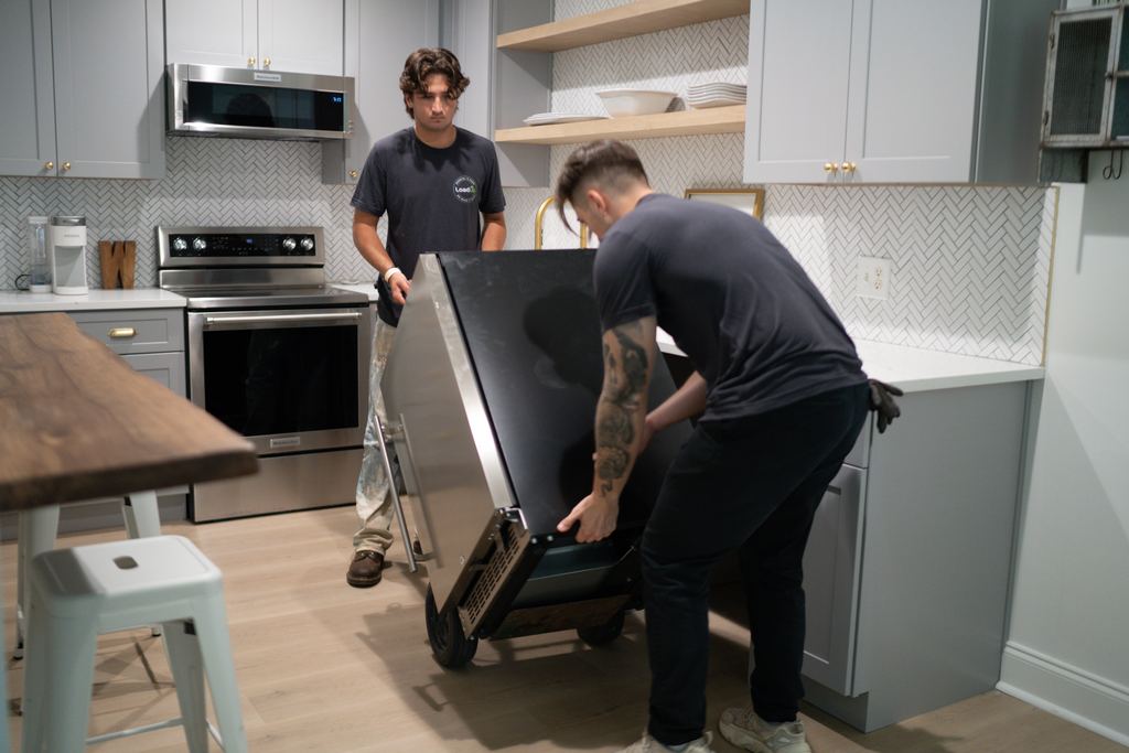 Two Loaders moving a large appliance on a hand truck through a kitchen
