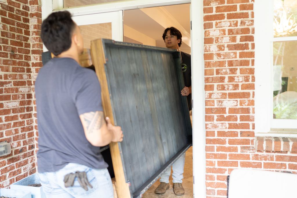 Two Loaders carrying a large wooden table top through a front doorway