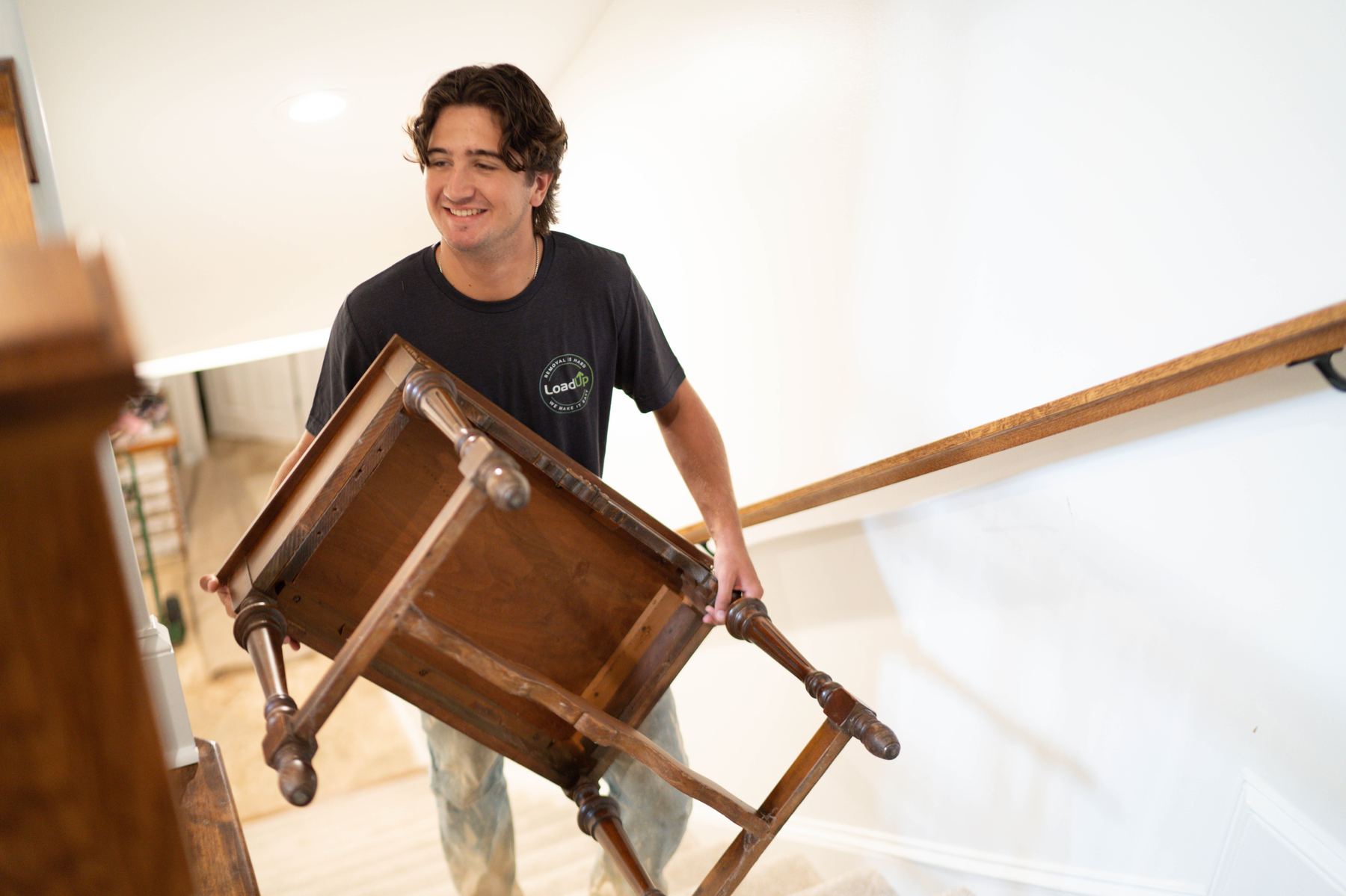 A smiling Loader carrying a wooden side table down the staircase