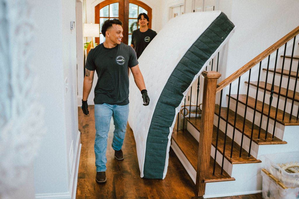 A smiling Loader carrying a mattress through a hallway during an in home pickup