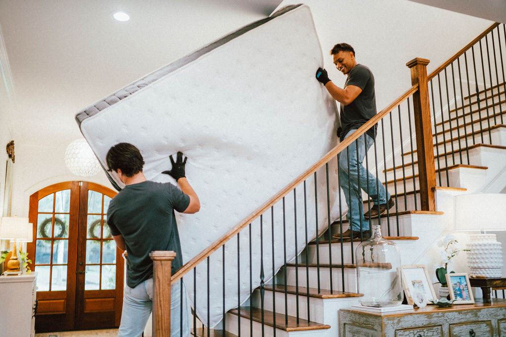 Two Loaders carrying a mattress down a staircase with gloved hands