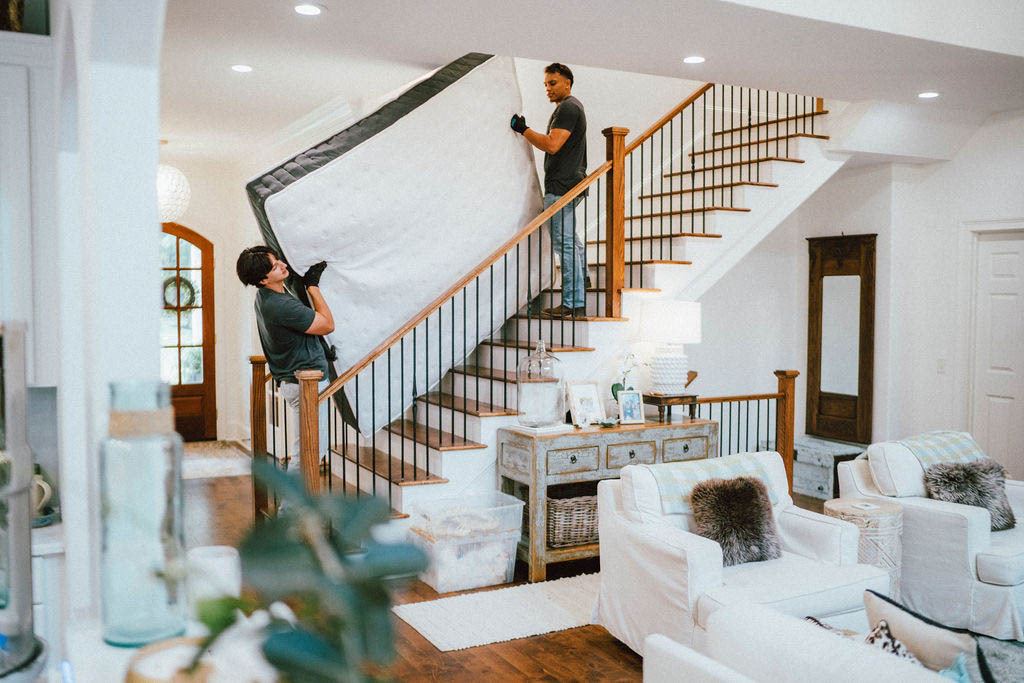 Loaders navigating a mattress down the stairs of a two story home