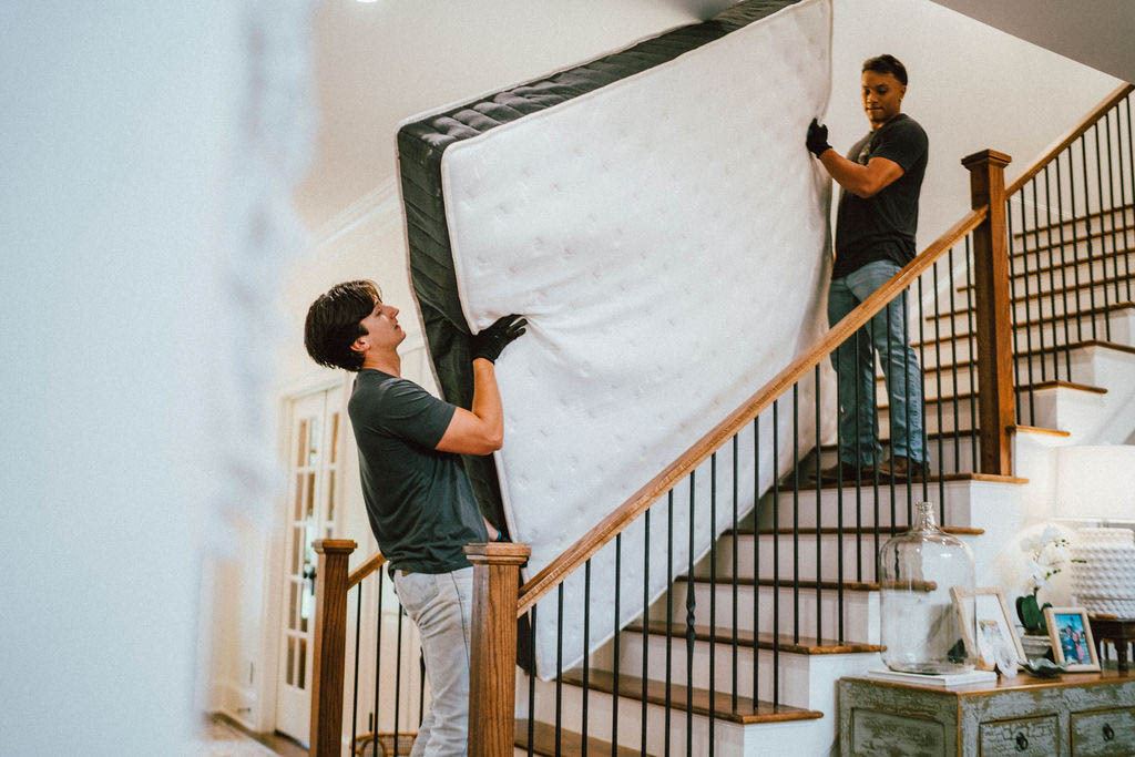 A Loader guiding a mattress down the staircase from below