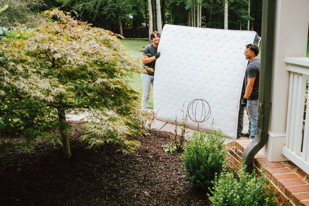 Loaders carrying a mattress along a garden walkway, long carries included