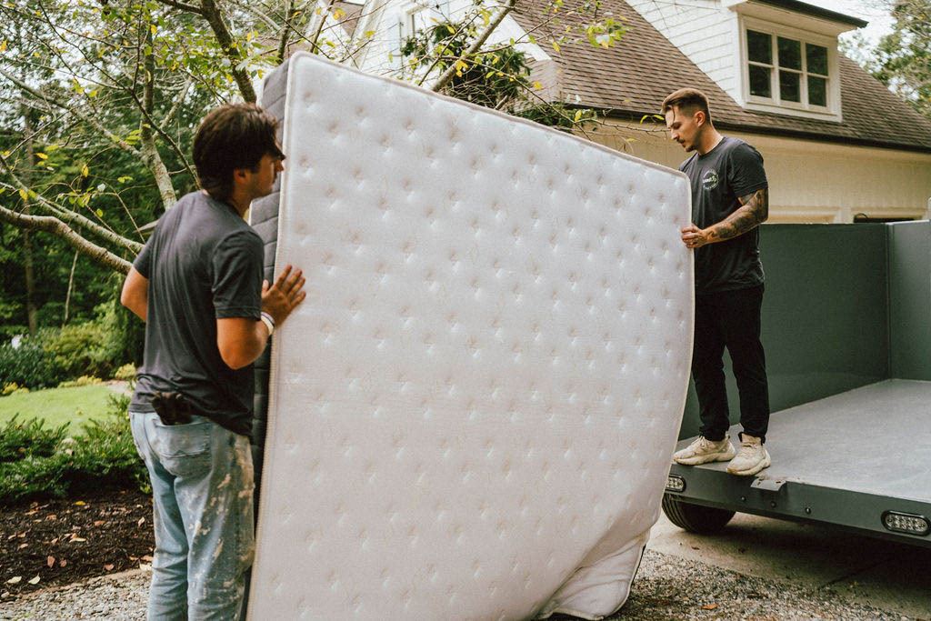 Loaders loading a used mattress onto a LoadUp trailer in a home driveway