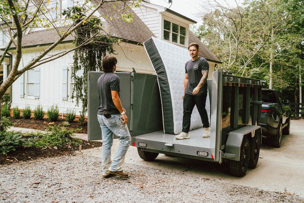 A Loader on the trailer bed receiving a mattress from his partner