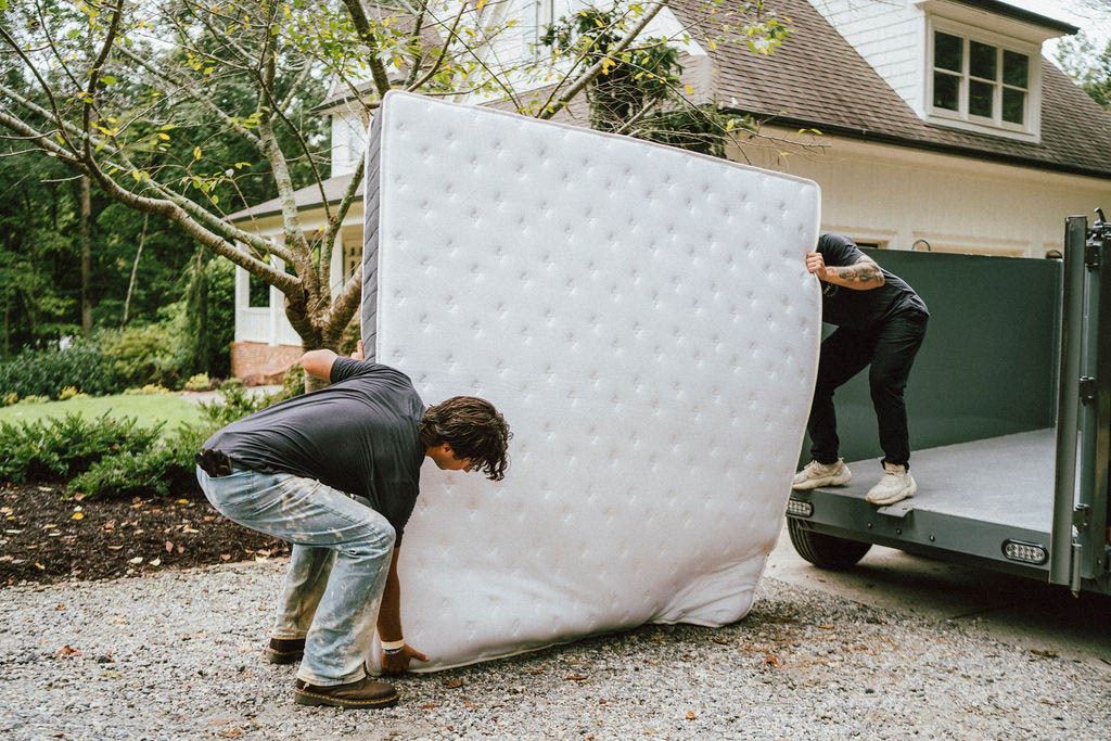 Loaders lifting a queen mattress onto the trailer ramp