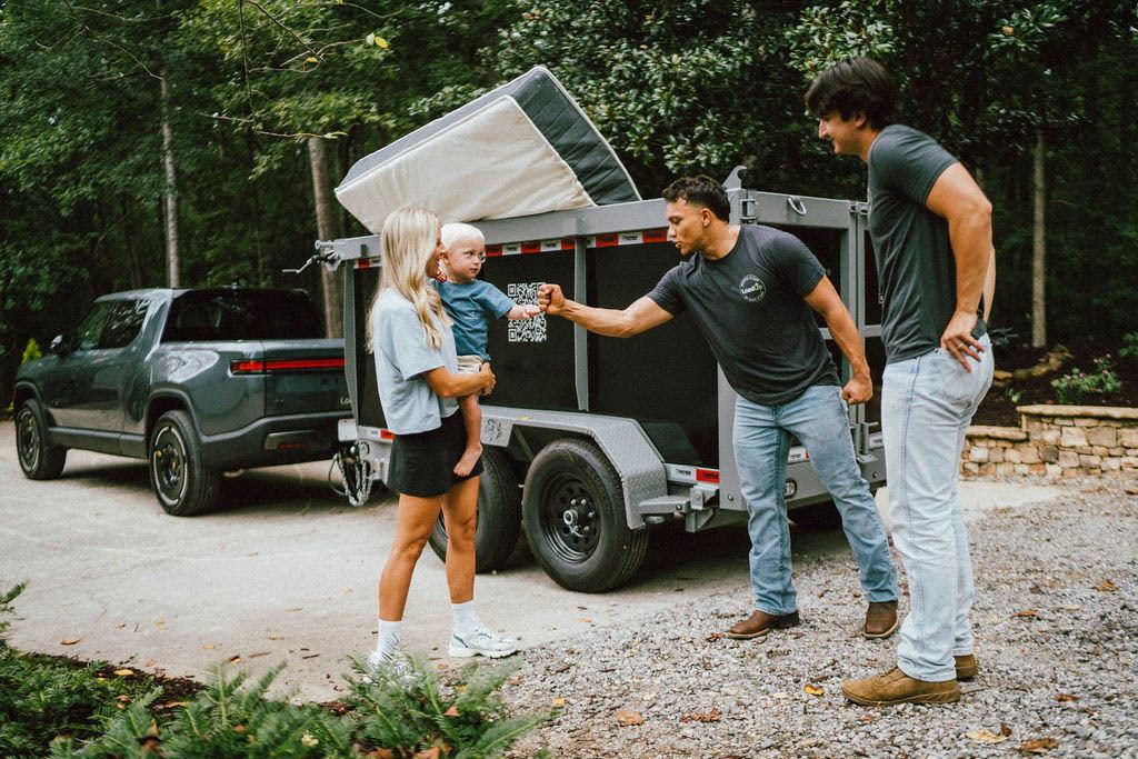 A Loader fist bumping a toddler while his mom watches, mattress loaded on the trailer behind them