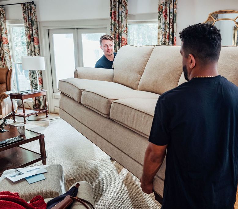 Two Loaders lifting a couch together in a living room