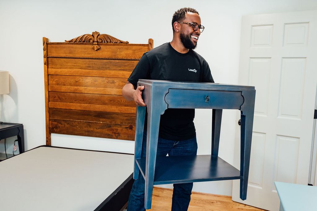 A Loader carrying a blue nightstand out of the bedroom