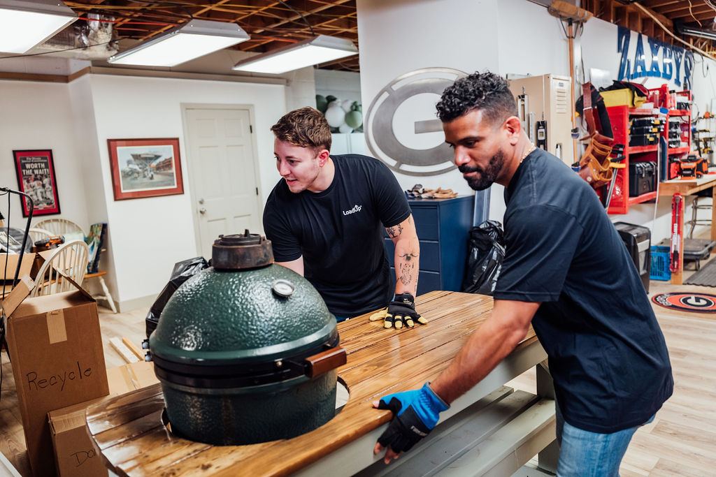 Two Loaders moving a wooden table carrying a ceramic grill out of a workshop