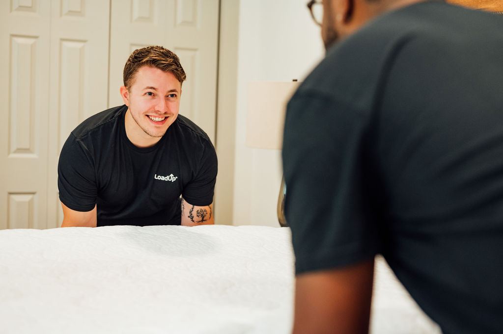 A smiling Loader in a LoadUp shirt preparing a mattress for pickup inside a customer bedroom